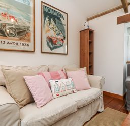 A sitting area with a beige sofa with cushions a wooden shelf a window with curtains and framed posters on the wall at Hay Loft Bolenowe Nr Portreath