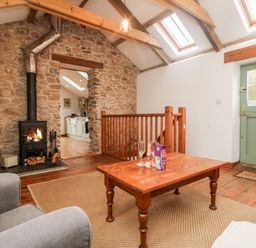 A seating area with a wooden coffee table and chairs near a wood burning stove and stone wall at Hay Loft Bolenowe Nr Portreath