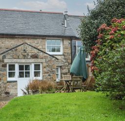 A stone cottage with a green lawn and outdoor wooden table and chairs at Trehan in St Ives