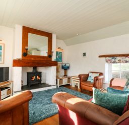 A living room with a wood burning stove under a large wooden framed mirror and leather armchairs at Trehan in St Ives