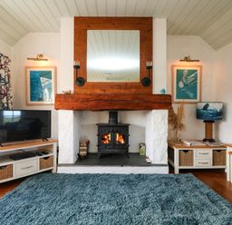 A room with a fireplace a wood stove a television a blue rug and cabinets at Trehan in St Ives