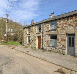 A stone cottage with two doors and windows on a quiet road near trees at Trevean in Portreath