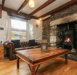 A living room with a leather sofa wooden coffee table stone fireplace and side cabinet at Trevean in Portreath