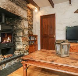 A living room with a stone fireplace and wood burning stove a wooden table with a lantern wooden door and a television on a wooden cabinet at Trevean in Portreath