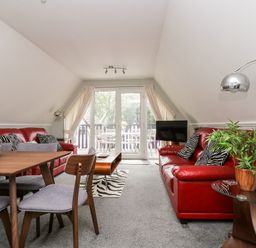 A living room with red sofas a dining table with chairs and glass doors leading to a balcony at Devine Lodge in Callington