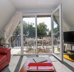 A living room with red leather sofas coffee table and a television next to glass doors leading to a deck with outdoor dining furniture at Devine Lodge in Callington