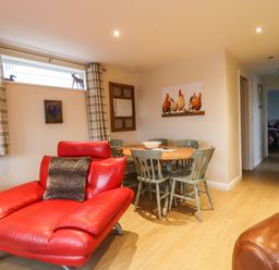 A dining area with a round wooden table and green chairs next to a living room with red leather chairs at The Old Hen Shed in Hainworth near Haworth
