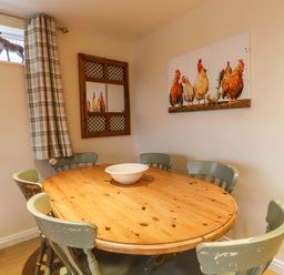A dining room with a round wooden table and six chairs with a bowl on the table at The Old Hen Shed in Hainworth near Haworth
