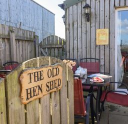 An outdoor patio with a wooden gate and a sign reading The Old Hen Shed with red chairs around a black table at The Old Hen Shed in Hainworth near Haworth