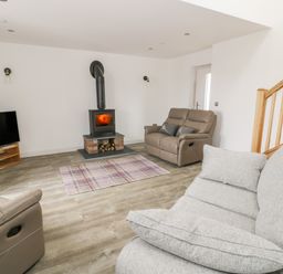 A living room with a wood burning stove two sofas a television on a wooden stand and a wooden staircase at Storws in Pentraeth