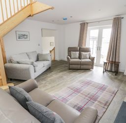 A living room with sofas wooden staircase and glass doors at Storws in Pentraeth