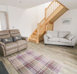 A living room with two sofas a plaid rug wooden staircase and a door at Storws in Pentraeth