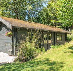 A single story cabin with a sloped roof surrounded by grass and trees at Pond Cabin in Stithians