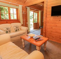 A living room with two sofas a wooden coffee table and a wall-mounted television at Pond Cabin in Stithians