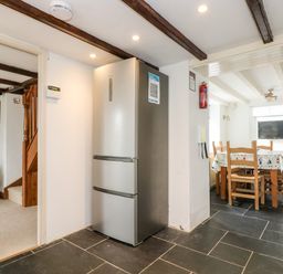 Kitchen area with a refrigerator next to a dining table and chairs at Forge Cottage in Sennen