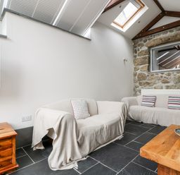 A sitting room with two sofas a wooden coffee table a small wooden cabinet and a stone wall at Forge Cottage in Sennen