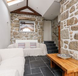 A seating area with two sofas a wooden table with a decorative bowl stone walls and black tiled floor at Forge Cottage in Sennen