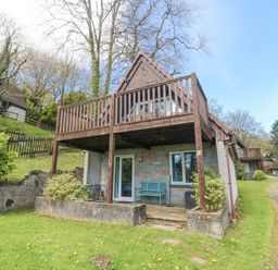 An outdoor view of a two-story wooden lodge with balcony and patio at Valley Lodge 44 in Callington