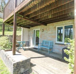 A covered wooden patio with a blue bench a table and chair outside a stone house at Valley Lodge 44 in Callington