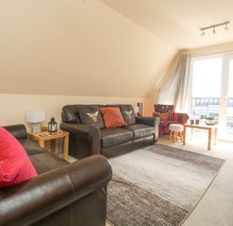 A living room with two brown leather sofas a red patterned armchair a wooden coffee table and large windows at Valley Lodge 44 in Callington