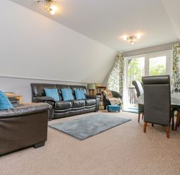 A living room with black leather sofas blue cushions a dining table and floral curtains at Valley Lodge 5 Callington