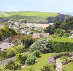 A coastal village with houses and a garden with a pond and flowers overlooking a beach and green hills at Windrush in Mawgan Porth