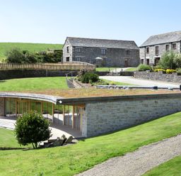 A stone modern building with grass roof near two traditional stone houses on a grassy landscape at Westhayes in Camelford