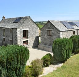 Two stone buildings with solar panels on the roofs surrounded by bushes and grassy land at Westhayes in Camelford
