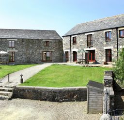 A stone built house and outbuilding with a gravel path grass yard and outdoor tables with umbrellas at Westhayes Camelford