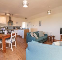 An open plan room with a kitchen area a wooden dining table with chairs and a seating area with sofas and a television at Kerensa ha-Kres in Sennen