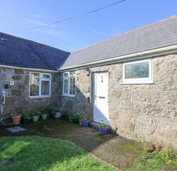 An exterior view of a stone house with doors windows and potted plants in a courtyard at Kerensa ha-Kres in Sennen