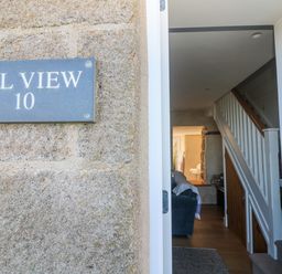 An entrance door open to a hallway with stairs and a living area at Bal View in St Just