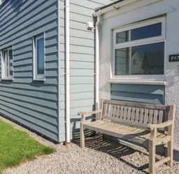 A wooden bench outside a house with blue siding and white walls at Penhaven in Crackington Haven