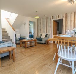 A living room and dining area with wooden floor wooden tables blue armchairs white chairs and a wooden dining table at Penhaven in Crackington Haven