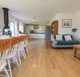 An open-plan kitchen and dining area with a wooden dining table and chairs a blue sofa and wooden coffee table at Penhaven in Crackington Haven