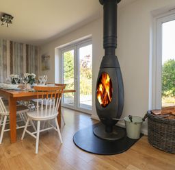 A dining room with a wooden table set with dishes and glasses next to a wood burning stove at Penhaven in Crackington Haven