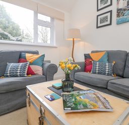 A living room with two gray sofas a wooden coffee table with magazines and a vase with yellow flowers at Mackerel Sky in Marazion