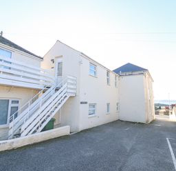 A white building with stairs and a parking area near the sea at Mackerel Sky in Marazion