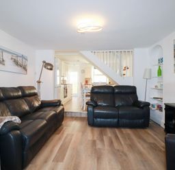 A living room with black leather sofas, wooden floor, floor lamps, paintings, and an open view to a kitchen and dining area at Alma House 2 in Perranporth