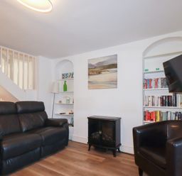 A living room with a black sofa black armchair bookshelf and a wall-mounted TV at Alma House 2 in Perranporth