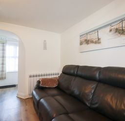 A living room with a black leather sofa a painting of a beach scene and a doorway leading to an entrance area at Alma House 2 in Perranporth