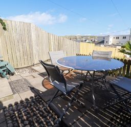 A patio area with a round glass table and four chairs surrounded by wooden fences at Alma House 2 in Perranporth
