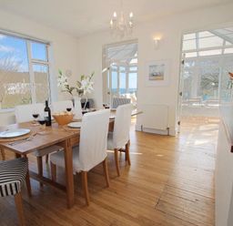 A dining area with a wooden table and chairs set with plates glasses and flowers at Porthcurno Bay View in Porthcurno