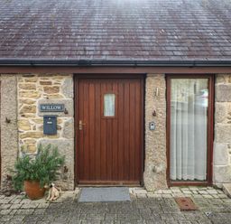 A stone house exterior with a wooden door and two windows with curtains and a plant in a pot at Willow in Falmouth