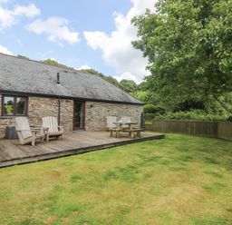 A wooden deck with chairs and a table next to a stone house and a grassy yard with a tree at Willow in Falmouth