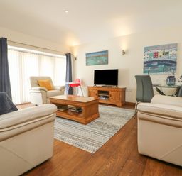 A living room with beige sofas a wooden coffee table a television on a wooden stand and a dining table with gray chairs at Willow in Falmouth