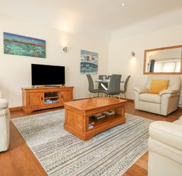 A living room with a television on a wooden stand a wooden coffee table several chairs and sofas and a dining table with four chairs at Willow in Falmouth