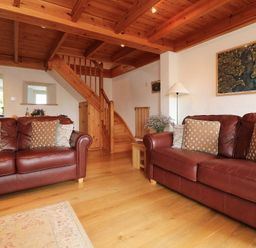 A living room with two brown leather sofas and wooden staircase at Halvosso in Falmouth