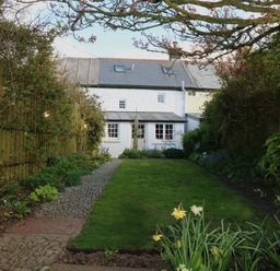 A garden with grass a stone path and flowers bordered by wooden fences at Halvosso in Falmouth