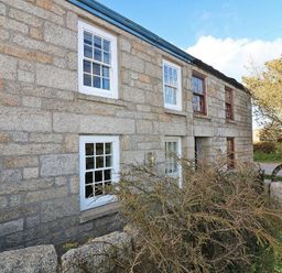 Stone cottage with white and brown window frames and shrubs in front at Halvosso in Falmouth